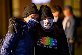 Masked protestors side hugging.