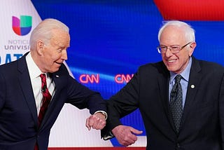 A photo of Joe Biden and Bernie Sanders elbow bumping each other at the 11th Democratic Party 2020 presidential debate.