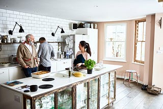 A photo of an Asian woman in the kitchen with her white husband and father-in-law.