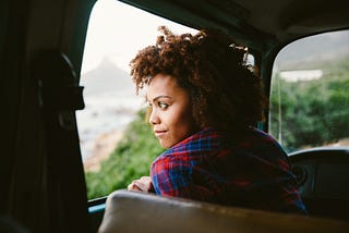 Black woman looking out the window of her car from the driver seat.