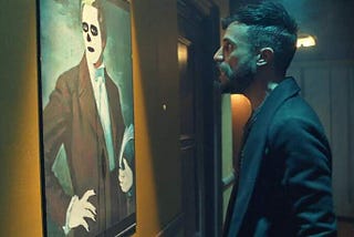 In a dim, eerily lit hallway, a young bearded man with a hip haircut scowls at a defaced painting of the LDS prophet Joseph Smith.