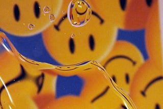 A photo of water droplets on glass with a reflection of upside down smiley face icons in the background.