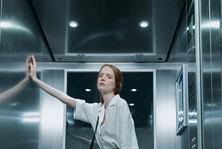 A low angle shot of a woman in black pants and white shirt standing inside the elevator