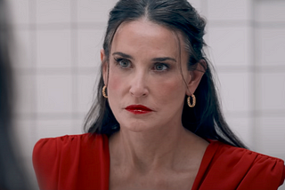 Demi Moore in red lipstick and red dress in front of a mirror in ‘The Substance.’