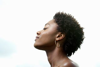 A photo of a black woman with her eyes closed, head tilted towards the sky, looking peaceful and serene.