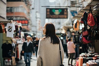 A photo of the back of a young Asian woman walking through a local market street in Hong Kong.