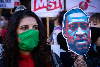 A woman wearing a face mask holds up a sign of George Floyd at a protest in Buenos Aires, Argentina.