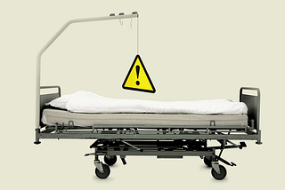 Side-view of a hospital bed with a metal bar above it; hanging from it is a triangular yellow caution sign.