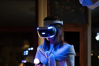 A woman is standing in a room with a VR headset on. It is nighttime.