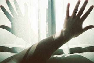 A photo of a hand against light with another shadow of a hand overlaid on the other side of the window.