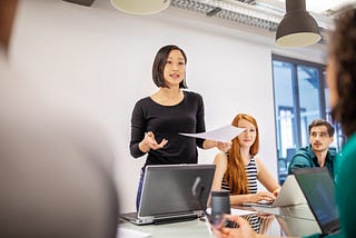 Asian businesswoman talking in front of co-workers giving a presentation.