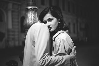 A Monochrome photo of a woman looking at the camera while a person is hugging her.
