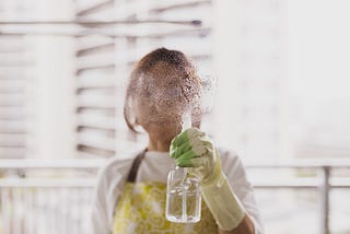 Woman spraying cleaning product in the air, obscuring her face.