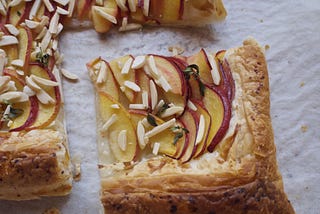 A tart topped with thinly-sliced peaches, sprinkled with slivered almonds.