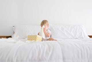 A photo of a baby covering his face with tissues that he’s taken out of a tissue box.