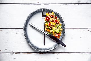 A fork and knife on a round plate in the position of clock hands, with salad in between as a symbol for intermittent fasting.