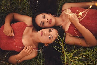 Two sisters laying on the grass next to each other.