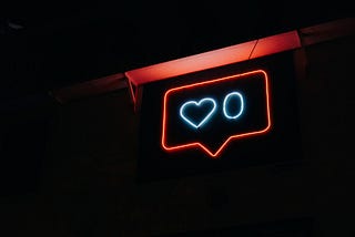 A red neon light signal hanging from a wall  which portraits a heart