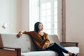 Asian woman sitting on her sofa looking out the frame.