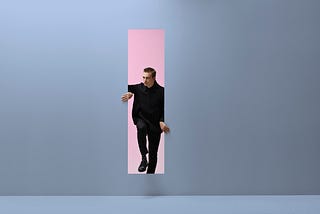 A masculine-appearing person emerging from a pink room into a blue room through a vertical rectangular opening in the wall.