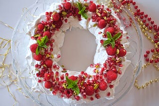 A wreath made of stiff sweet white vegan meringue sits on a plate and is decorated with red berries and leaves