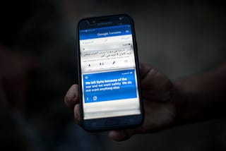 Photo of a man holding  his mobile phone that says “We left Syria because of war and we want safety” on Google Translate.