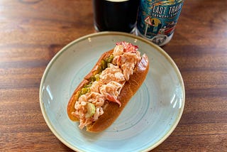 Photo of a lobster roll on a plate with a cup of beer next to it.