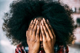 A photo of a black woman covering her face with her hands.