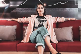 Latina woman in rolled up jeans and silk jacket sitting on a red couch looking confident and in charge
