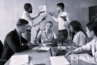 A group of multi-gender; multi-racial people is business attire sitting and standing around a conference table having a very animated dicussion.