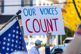 Protestor holding a sign that says “OUR VOICES COUNT.”