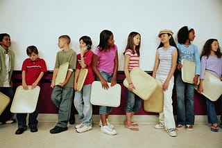 Middle school kids holding their trays wait in a school lunch line.