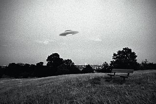 Grainy black-and-white photo of a UFO flying over a park bench overlooking an urban scene in the distance.