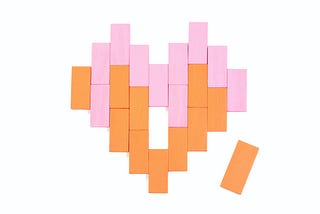 Orange and pink rectangular blocks arranged in the shape of a heart with one piece missing (an orange one next to the heart)