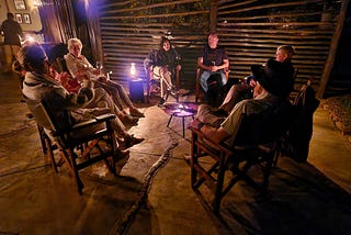 A group of people sitting on deck chairs around a campfire and a lantern