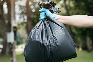 Close up of Large green trash bag held by someone wearing a blue latex glove.