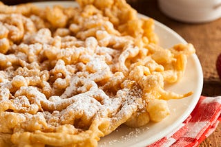 A plate of a powdered sugar-dusted funnel cake, on a red-and-white gingham cloth.