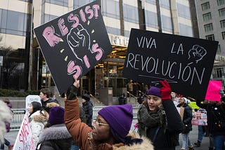 Marchers hold signs that say “Resist Sis” and “Viva La Revolucion” in front of Trump International Hotel on January 19, 2019