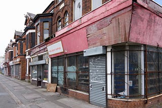 A row of shops that are boarded up on a street corner.