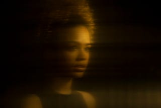 Distorted gold-tinted reflection of a young Black woman.