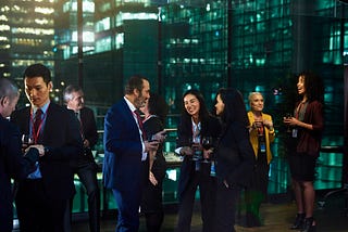 A photo of business people networking in an office building with glass windows at night.