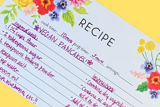 A printed recipe card with a vegan pancake recipe handwritten in pink ink.