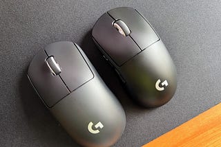 Two black mice with white accents and Logitech logos sit on a black desk mat. The left model is a first gen Superlight, and the right model is the brand new Superlight 2C or “Compact.”