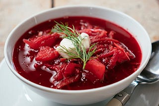 A bowl of borscht topped with a spring of dill and a dollop of sour cream.