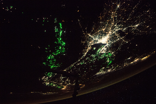 The Andaman Sea and Gulf of Thailand as viewed from the International Space Station. Photo has green and white lights lit up across the world, which is otherwise dark.