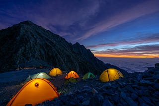 A picture of a campsite at nightfall, with several brightly-colored tents illuminated from within.