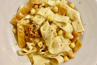 A plate of wide pasta topped with fried pasta and chickpeas.