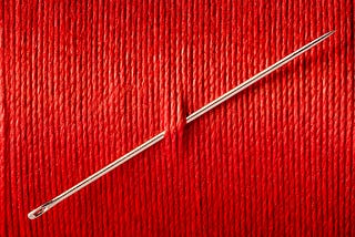 A needle stuck through a wall of red thread.