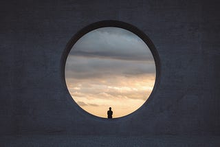 A person looking at a cloudy sky, sitting in a circular window that’s almost 10 times taller than them.