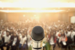 A microphone in the foreground with a large audience in the background.